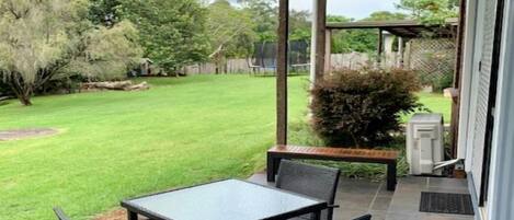 Un patio con mesa y sillas, un área cubierta y un césped.