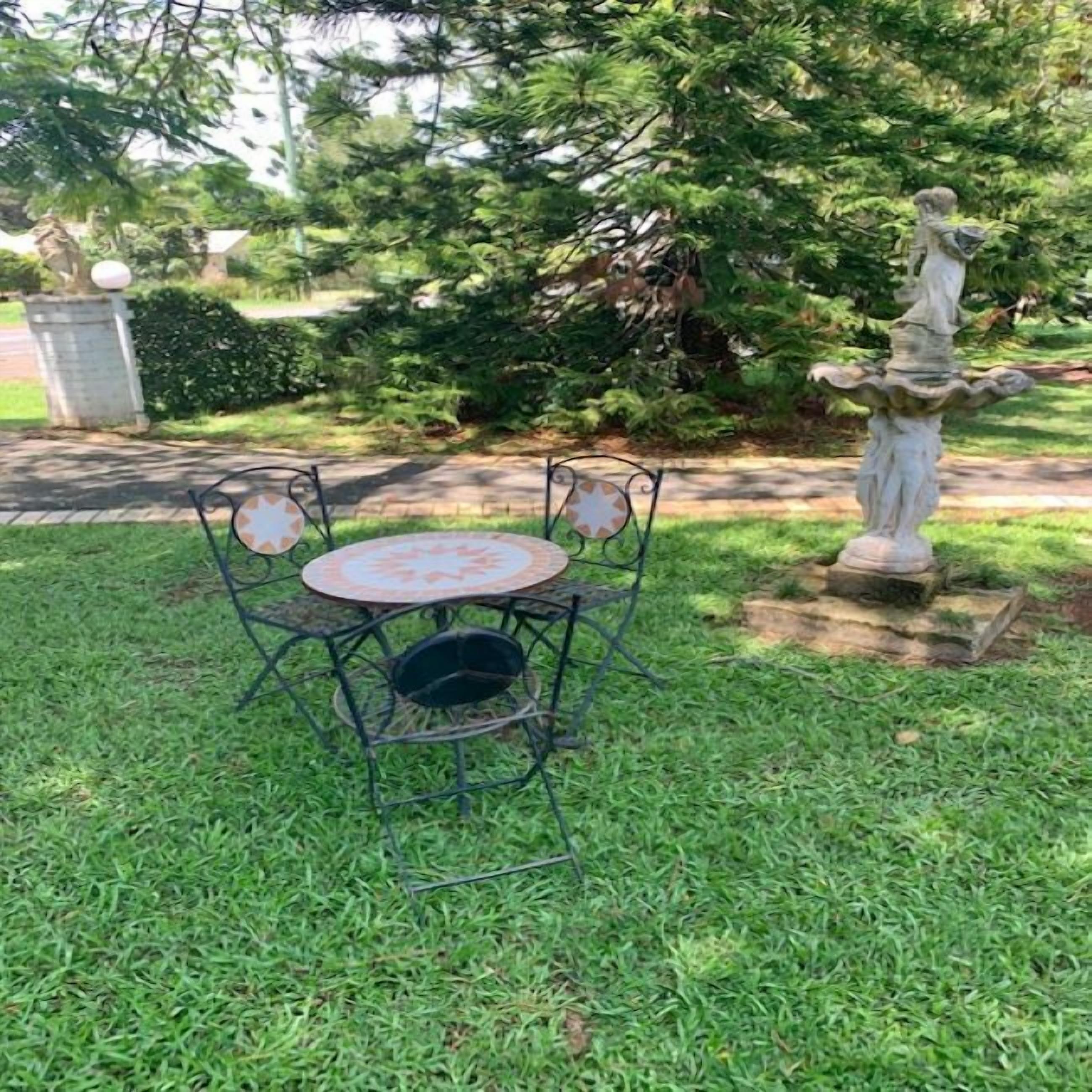Un pequeño patio al aire libre con una mesa redonda y cuatro sillas, rodeado de césped y una estatua.