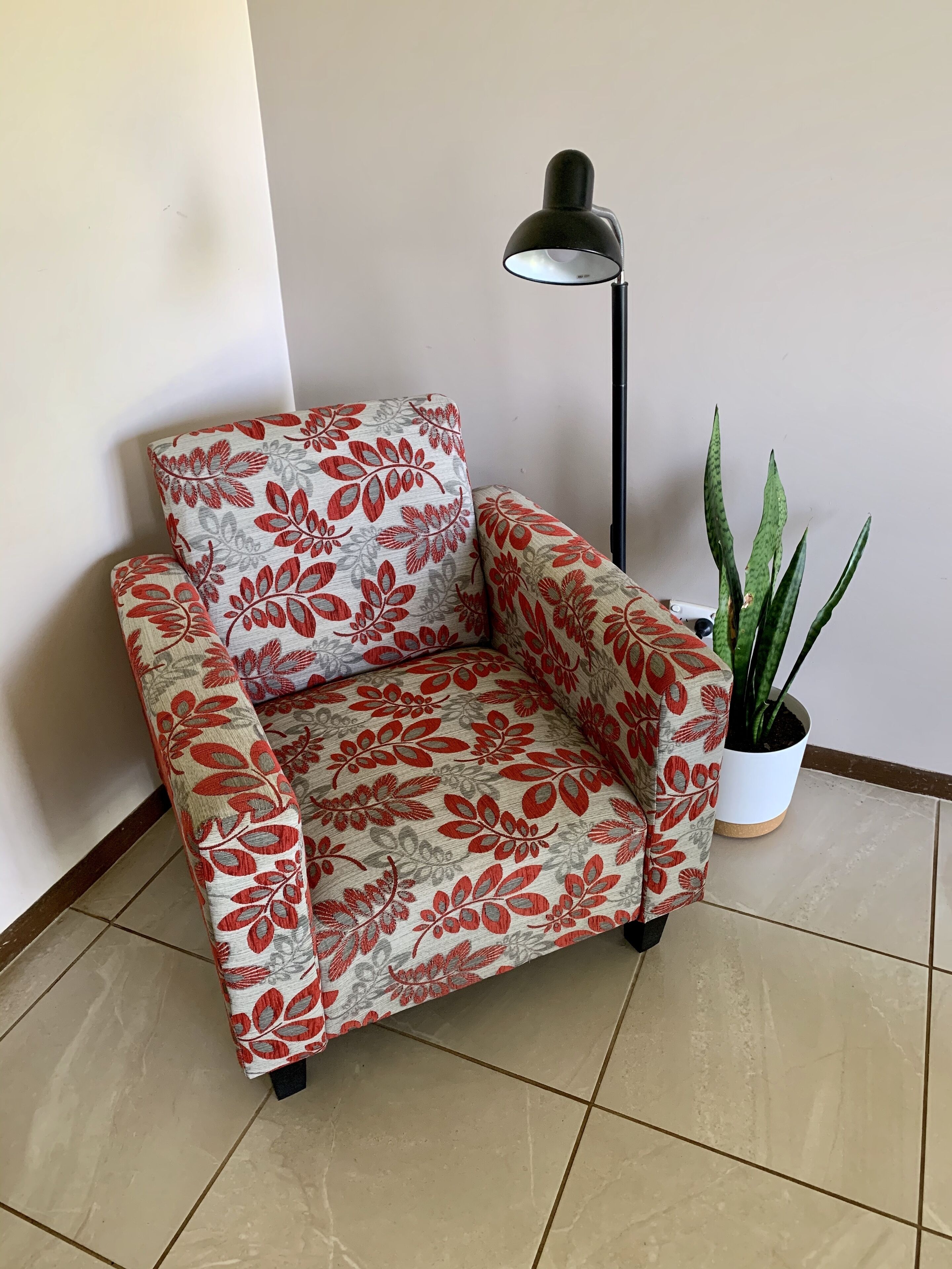 Una cadira amb dibuixos florals, una làmpada de peu i una planta en test.
