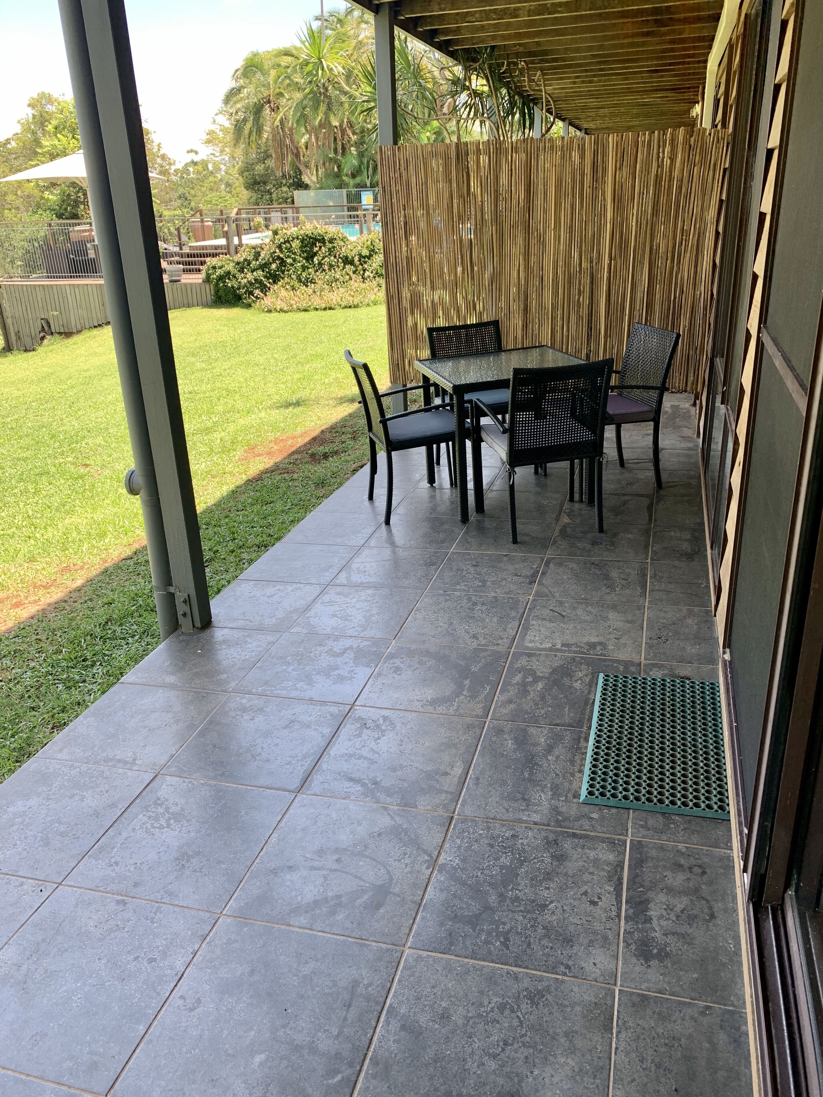 A covered patio area with a table and chairs, a grassy lawn, and a bamboo fence.