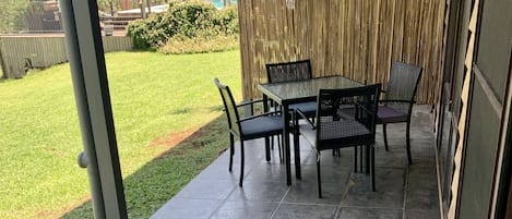 A covered patio area with a table and chairs, a grassy lawn, and a bamboo fence.