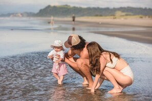 A beach scene with a family of three, including a child, in shallow water. - Ōhope Beach TOP 10 Holiday Park (Ohope)