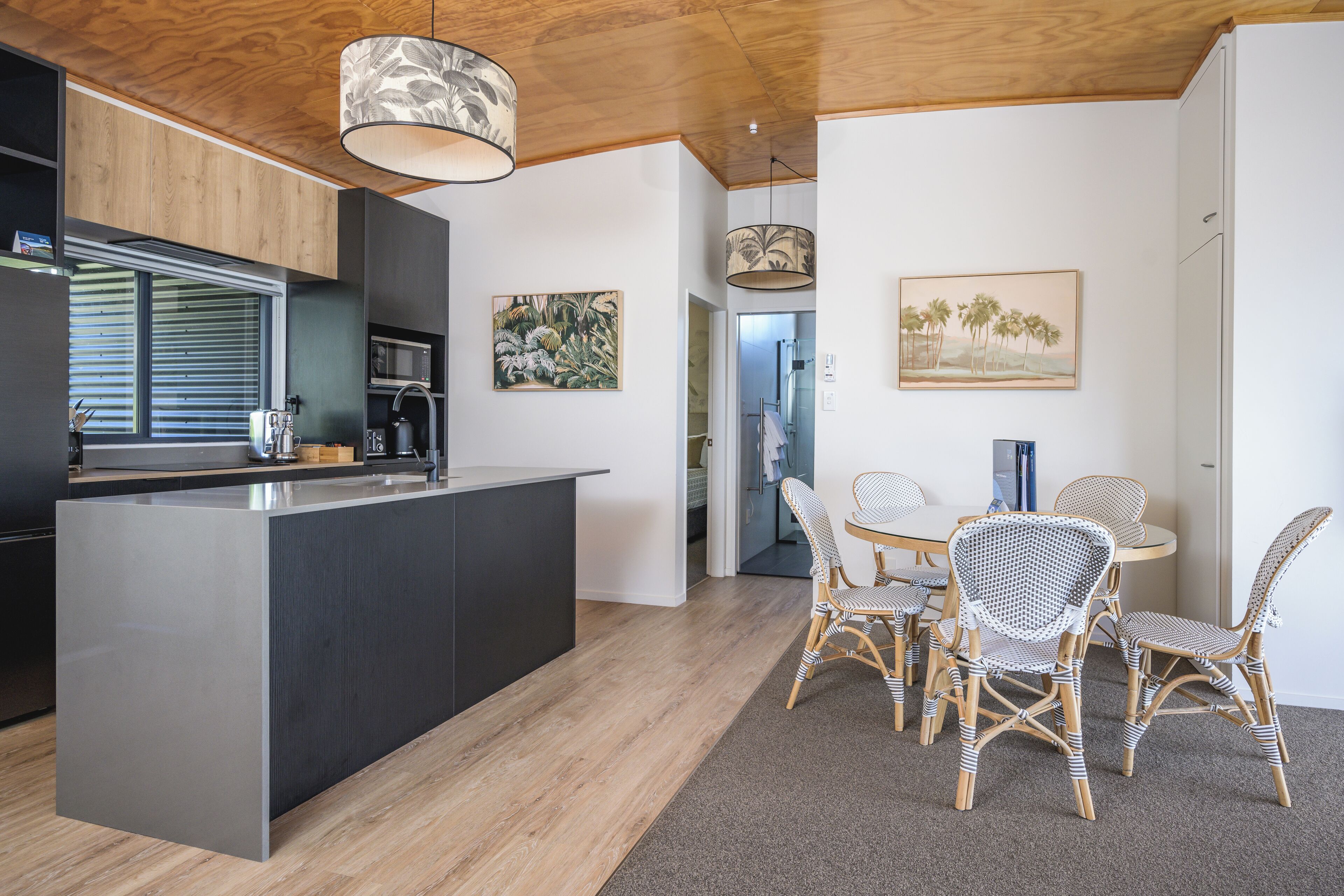 A modern kitchen with a central island, dining area with wicker chairs, and artwork on the walls.
