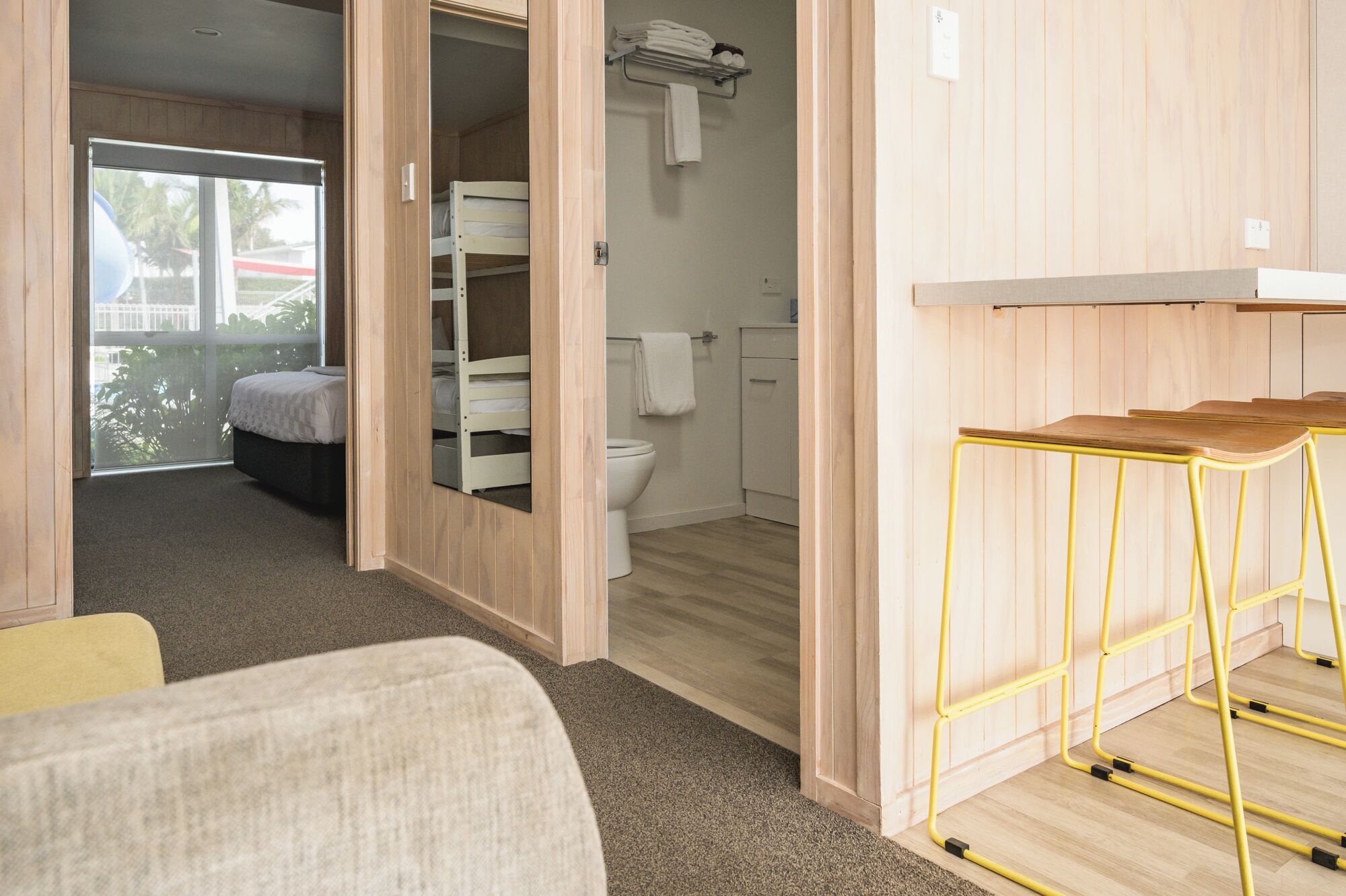 A compact room with a bunk bed, a small bathroom, and a yellow metal stool.
