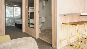 A compact room with a bunk bed, a small bathroom, and a yellow metal stool.