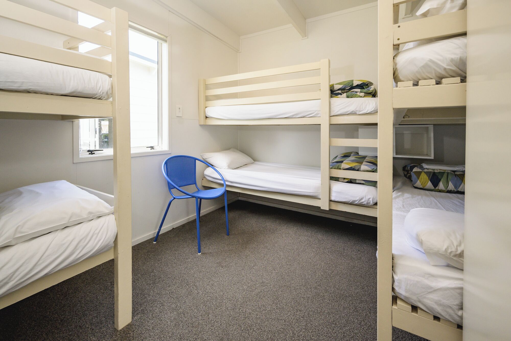 Un dormitorio con literas, una ventana y una silla azul.