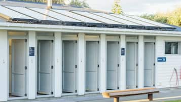 Une rangée de toilettes publiques mobiles blanches, dotées de portes numérotées, avec un banc à l’extérieur et un panneau solaire sur le toit.