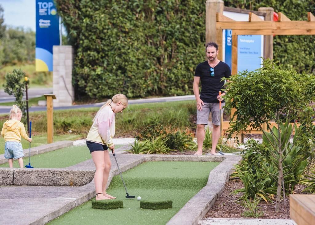 A miniature golf course with a green putting area, a wooden structure, and a sign in the background.