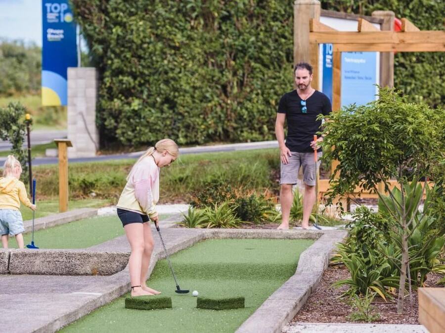A miniature golf course with a green putting area, a wooden structure, and a sign in the background.
