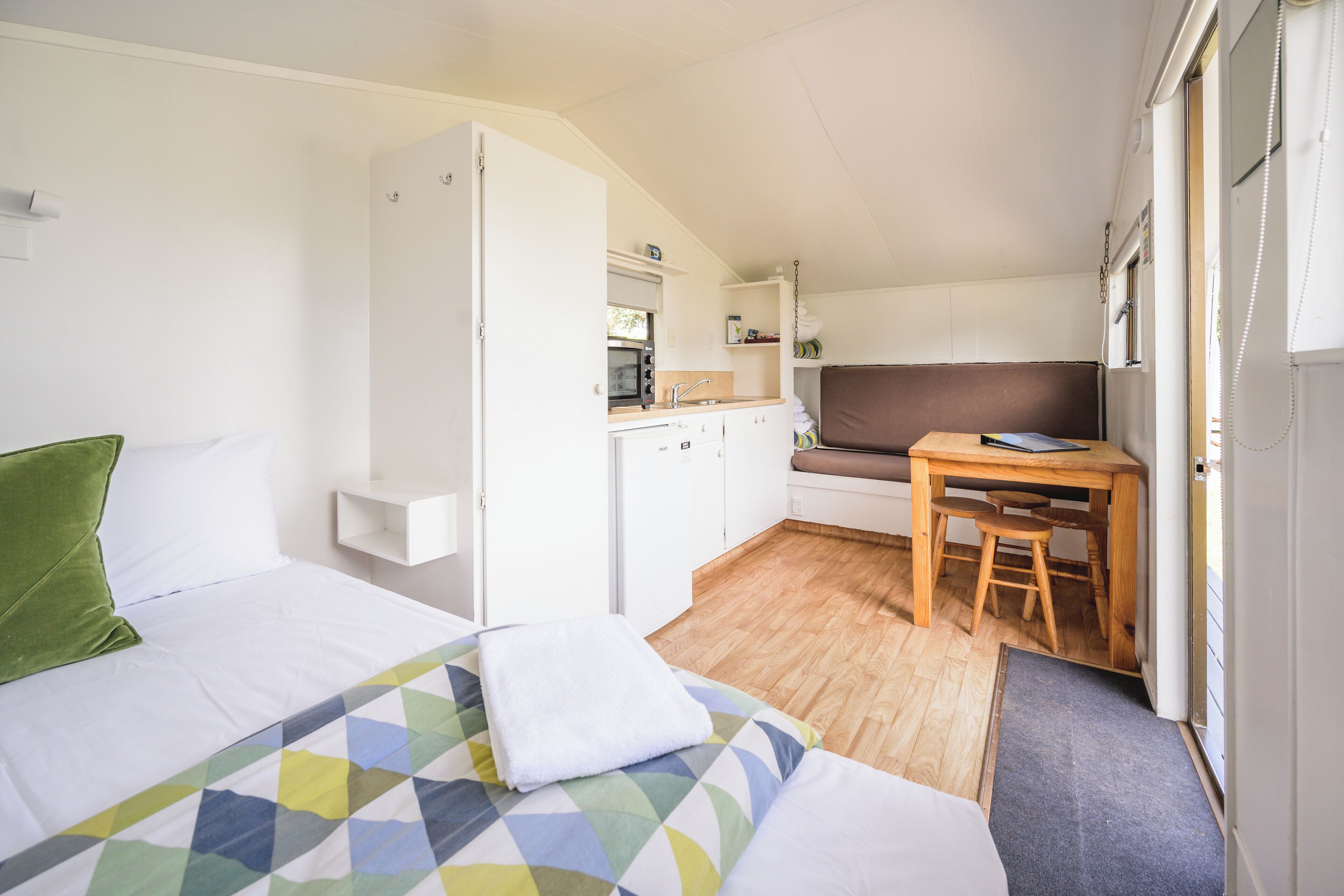 A compact room with two beds, a kitchenette, a dining area, and a small window.