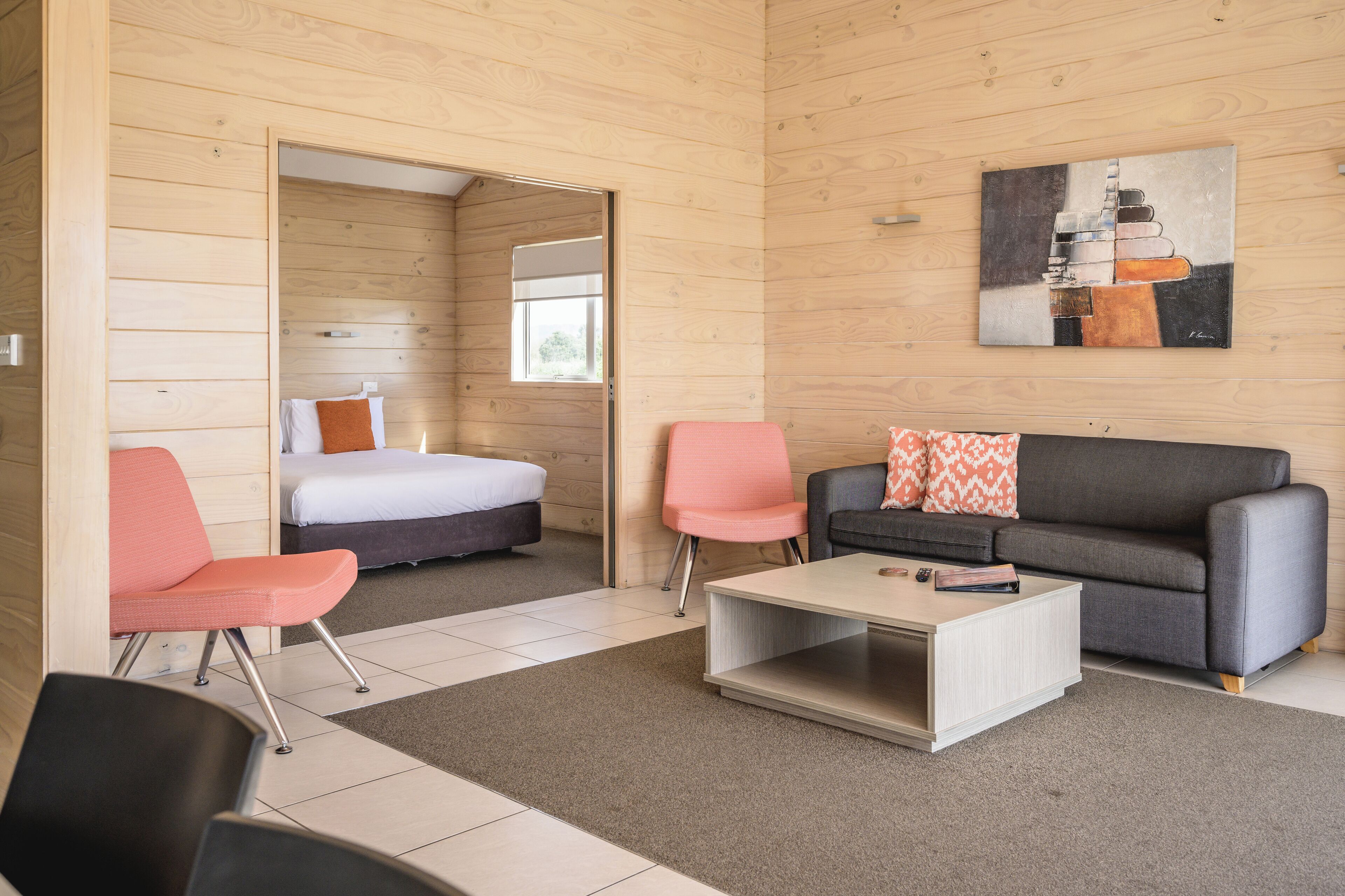 Een moderne hotelkamer met een houten inrichting, een bed, een bank, twee stoelen en een salontafel.