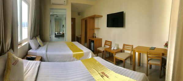 Habitación de hotel con dos camas, televisión, escritorio y sillas, y baño visible a través de una puerta abierta.