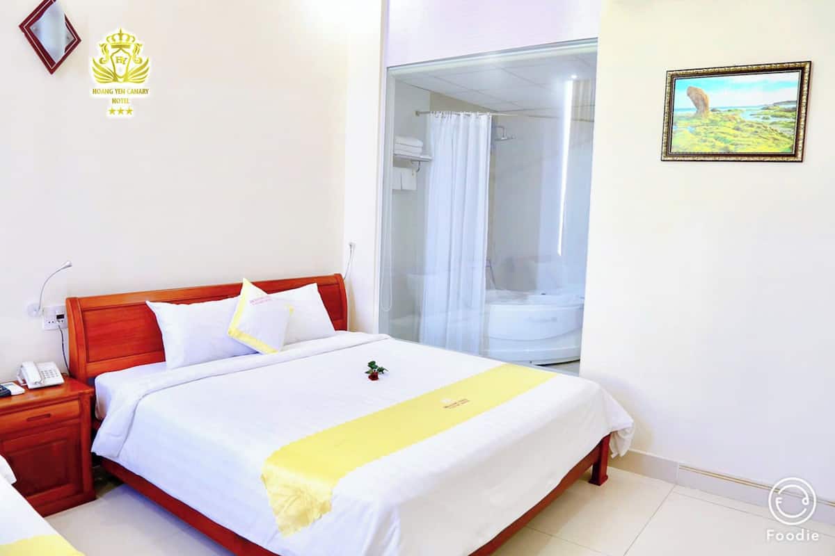 Une chambre d’hôtel avec un lit, une table de chevet avec un téléphone, un espace douche et un tableau encadré au mur.