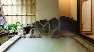 Un espace de sources chaudes agrémenté de murs en pierre, de paravents en bambou et d’un sol carrelé.