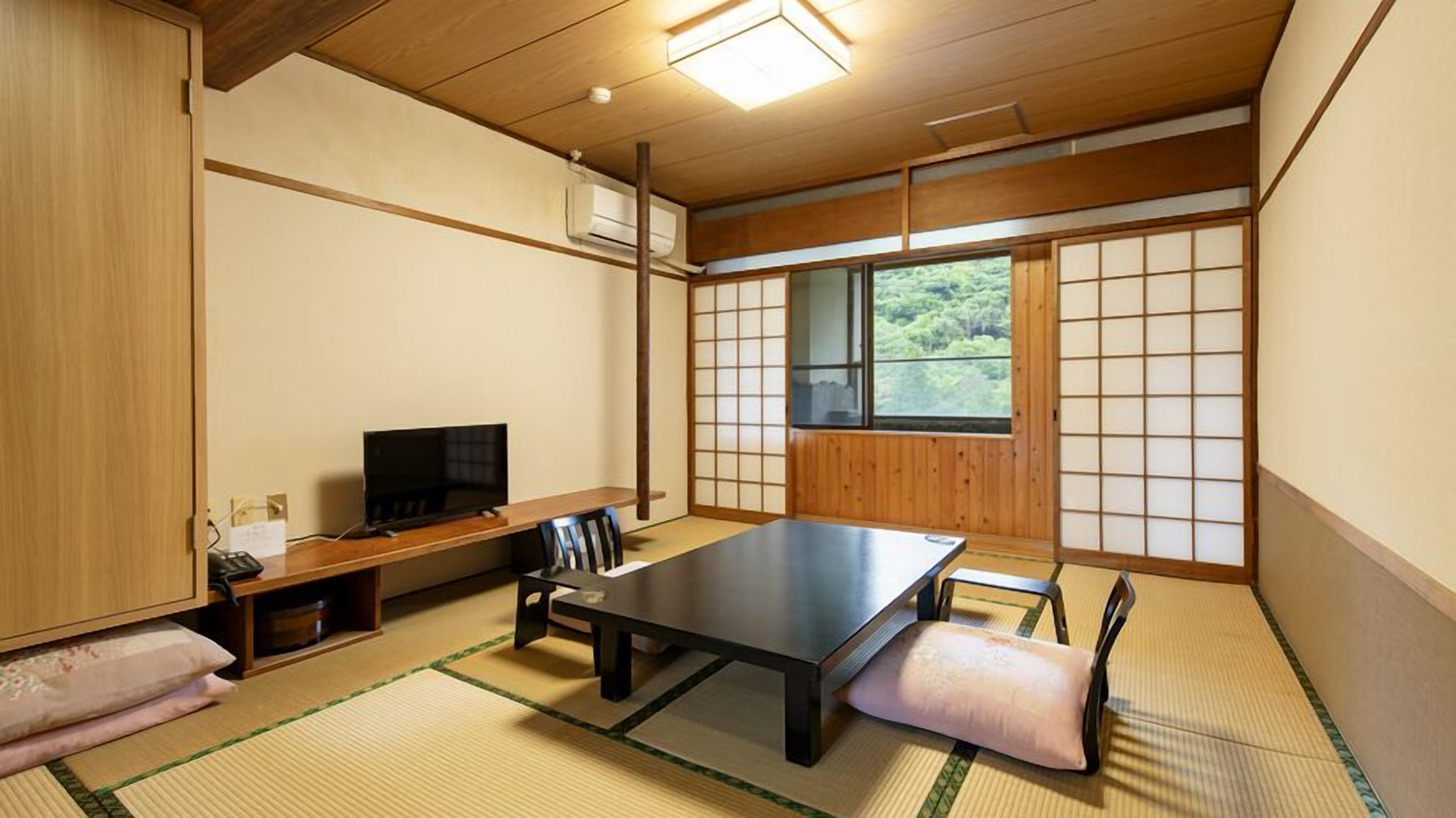 Ein traditioneller japanischer Raum mit Tatami-Boden, einem niedrigen Tisch, einem Fernseher und Schiebetüren.