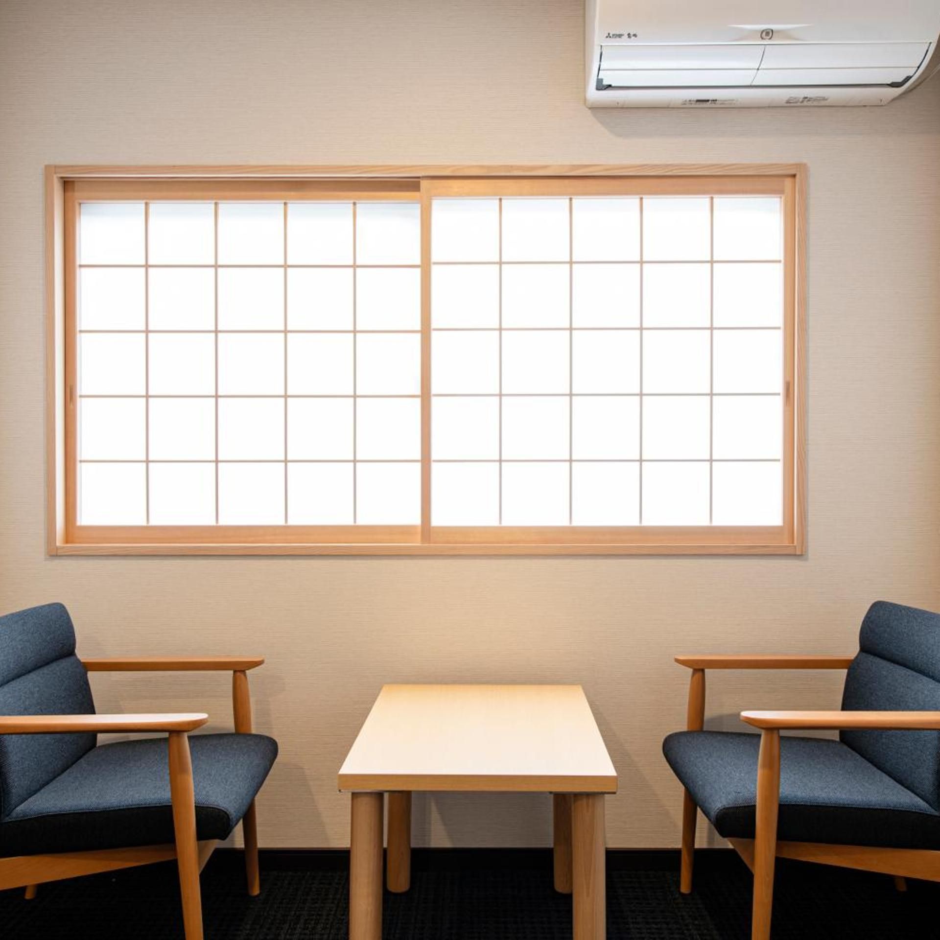 Una habitación con un ventanal grande, dos sillas y una mesa.