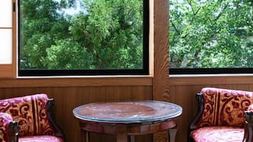 A room with two wooden chairs with cushioned seats and backs, a small round table, and a large window with a view of trees.