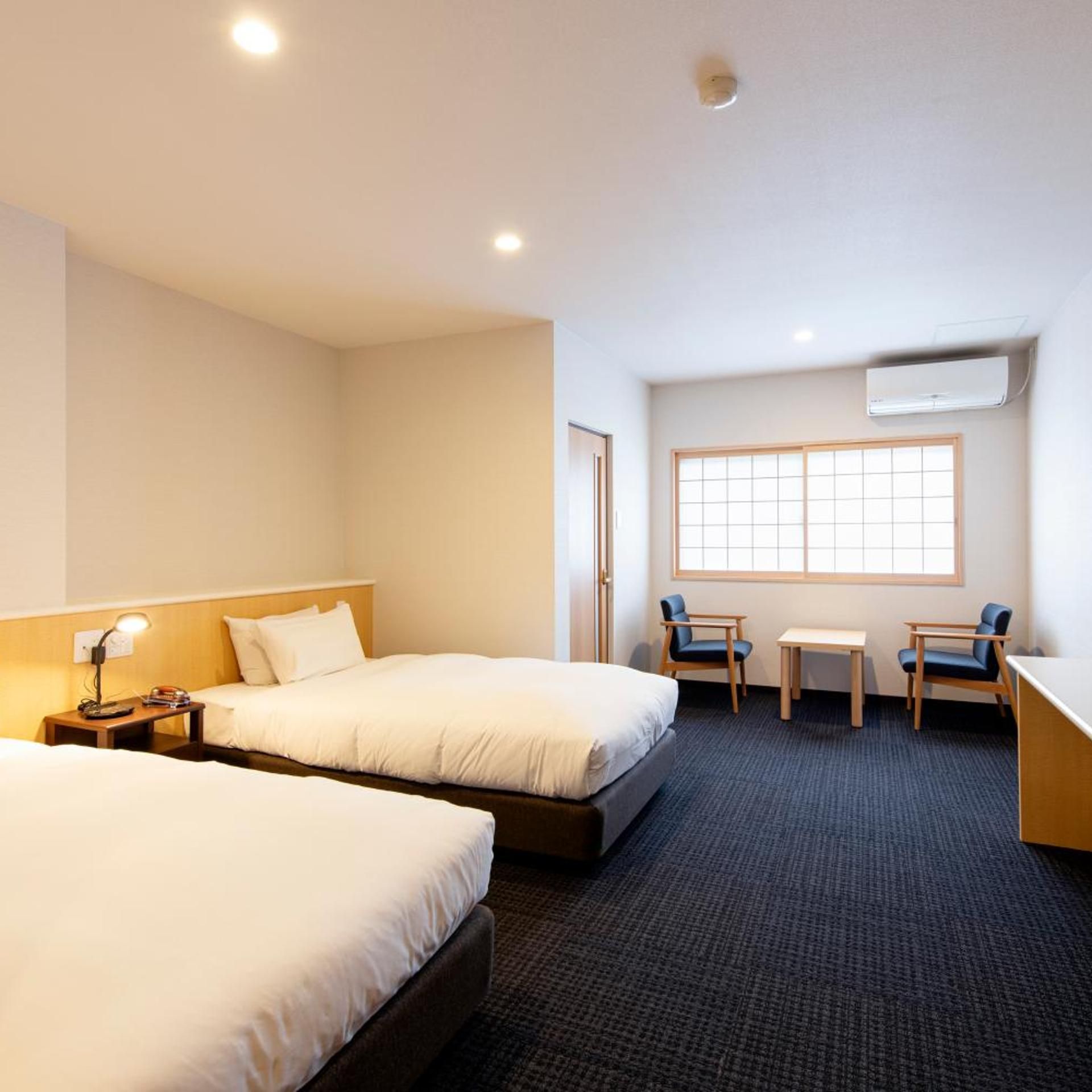 Quarto de hotel com duas camas, uma escrivaninha, uma cadeira e uma janela.