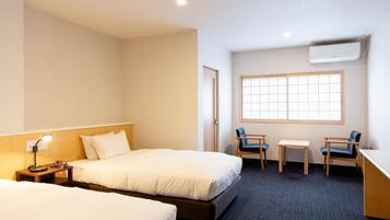 Quarto de hotel com duas camas, uma escrivaninha, uma cadeira e uma janela.
