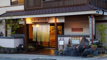 Un edificio japonés tradicional con fachada de madera, un sendero de piedra que conduce a la entrada y un letrero con caracteres japoneses.