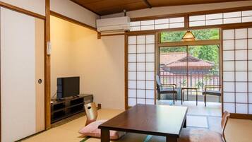 A traditional Japanese room with tatami flooring, a low table, a television, and sliding doors leading to an outdoor area.