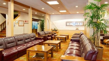 Un hall d’hôtel avec des canapés en cuir, des tables en bois et un escalier.
