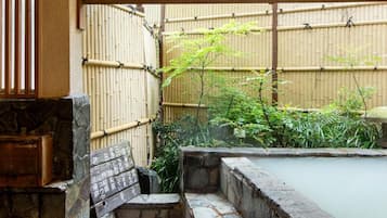 Un giardino tradizionale giapponese con una vasca termale in pietra, un recinto di bambù e una struttura in legno.