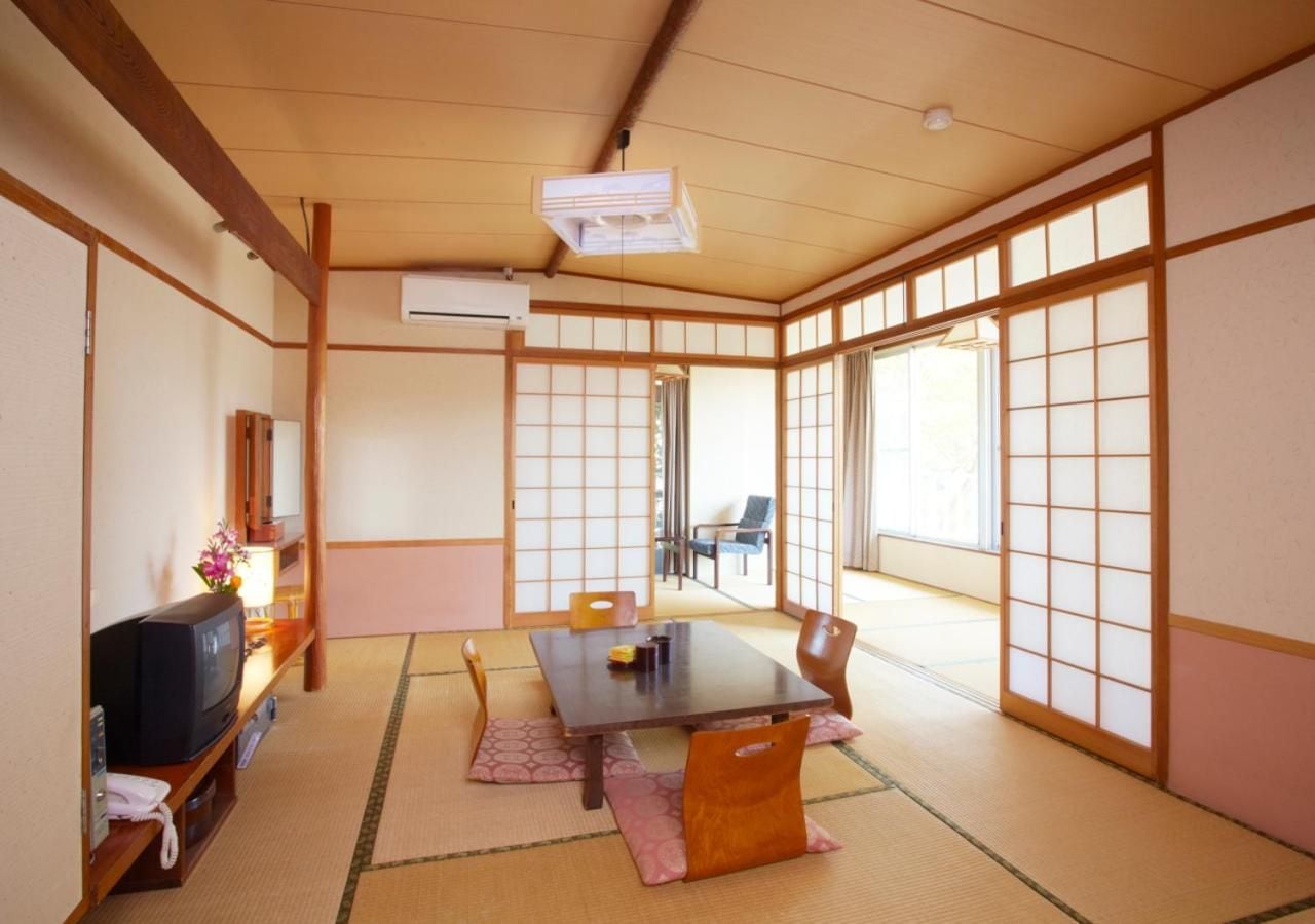 Una habitación japonesa tradicional con suelo de tatami, una mesa baja, un televisor y puertas correderas.