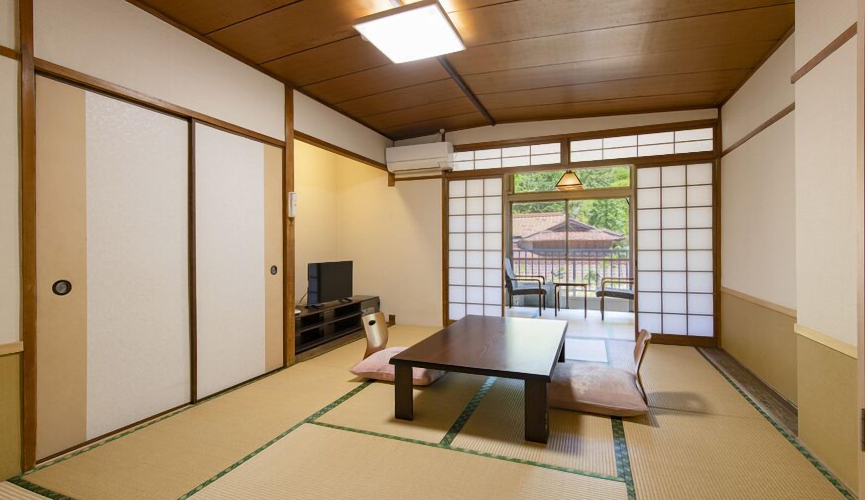 Ein traditioneller japanischer Raum mit Tatami-Böden, einem niedrigen Tisch, einem Fernseher und verschiebbaren Türen.