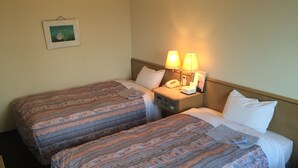 Een hotelkamer met twee bedden, elk voorzien van beddengoed met een patroon, een nachtkastje met een lamp, een telefoon en een ingelijst schilderij aan de muur.