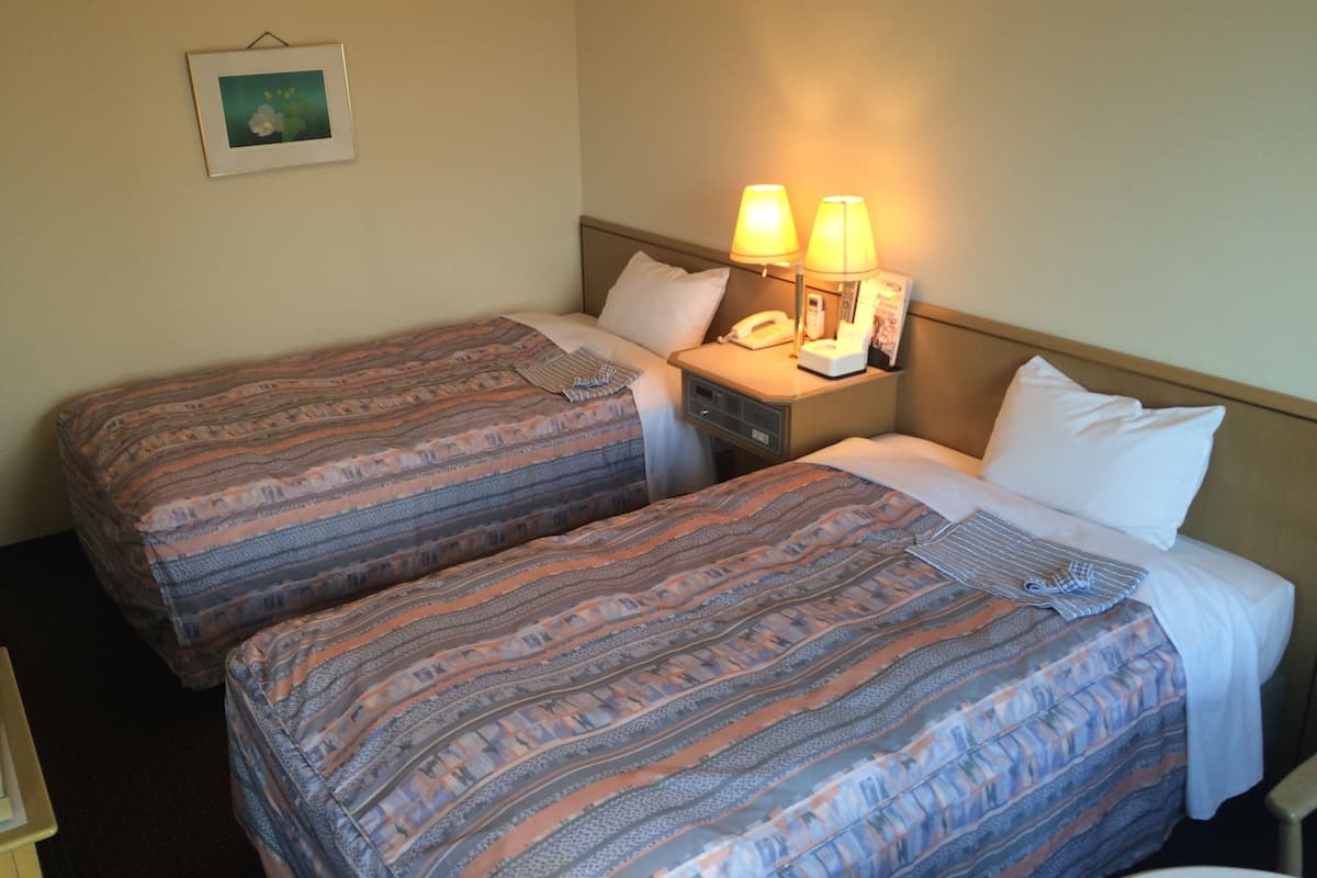 Ein Hotelzimmer mit zwei Betten, jeweils mit gemusterten Bettbezügen, einem Nachttisch mit Lampe, Telefon und einem gerahmten Bild an der Wand.