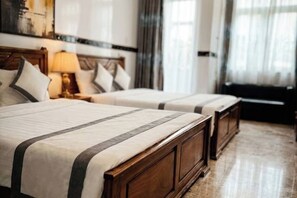A hotel room with two beds, wooden headboards, a nightstand with a lamp, and a large window with curtains. - CT Morning Hotel (Can Tho)