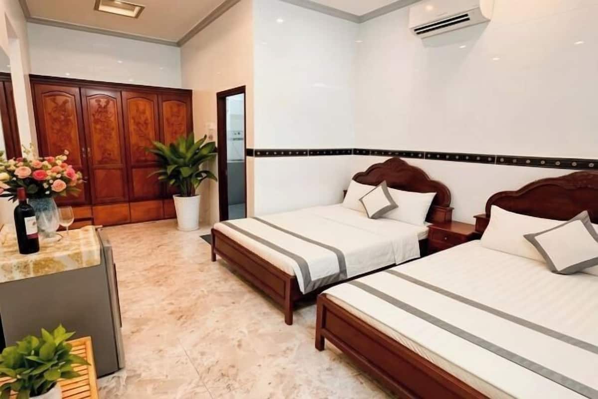 Une chambre d’hôtel avec deux lits, une armoire en bois, un sol en marbre et un comptoir de réception agrémenté d’une plante.