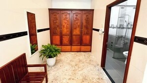 Un baño con armario de madera, un banco, una planta en maceta y un box de ducha de cristal.