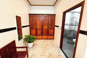 Un baño con armario de madera, un banco, una planta en maceta y un box de ducha de cristal.