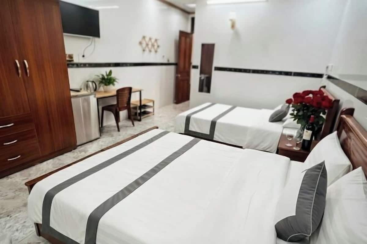 Une chambre d’hôtel avec deux lits, un bureau, une chaise, une télévision et une plante.