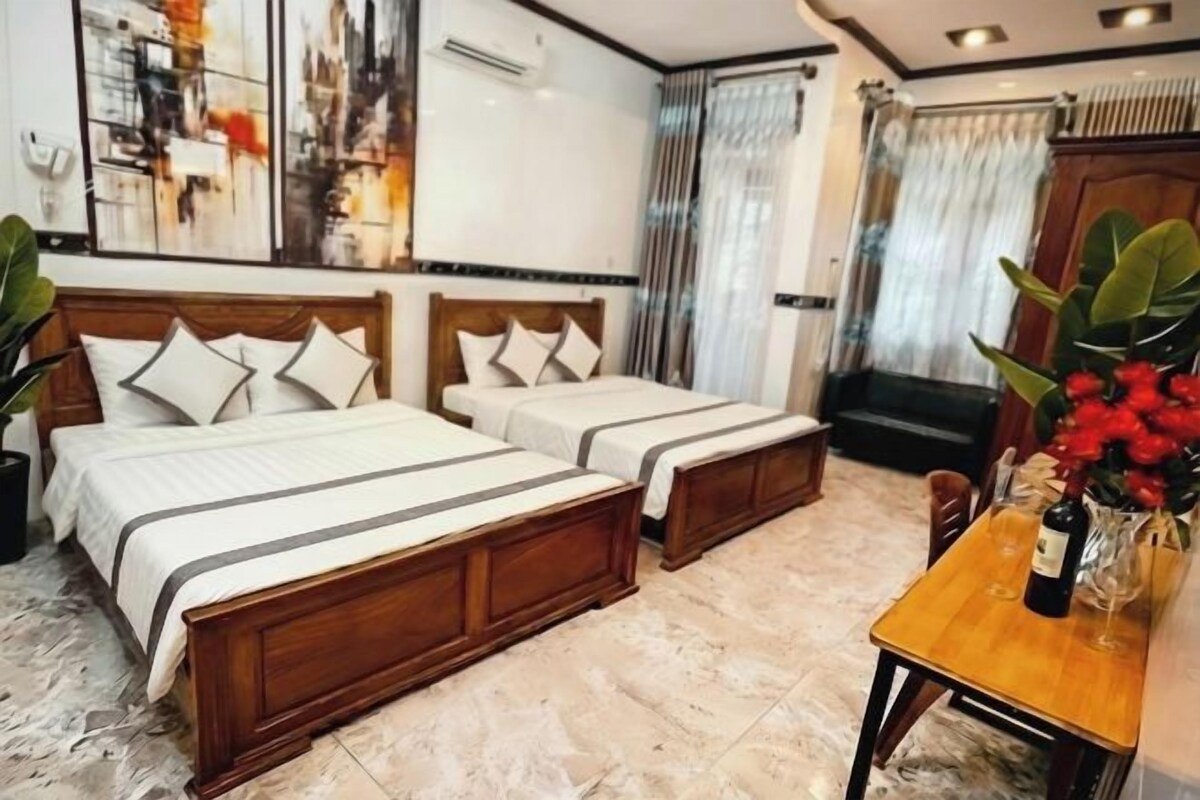 A hotel room with two wooden beds, a marble floor, a wooden table with a bottle and glass, and a large abstract painting on the wall.