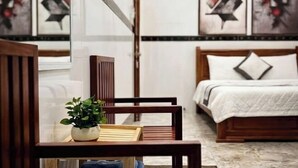 A hotel room with a wooden bed, a bedside table with a plant, and abstract wall art. - CT Morning Hotel (Can Tho)