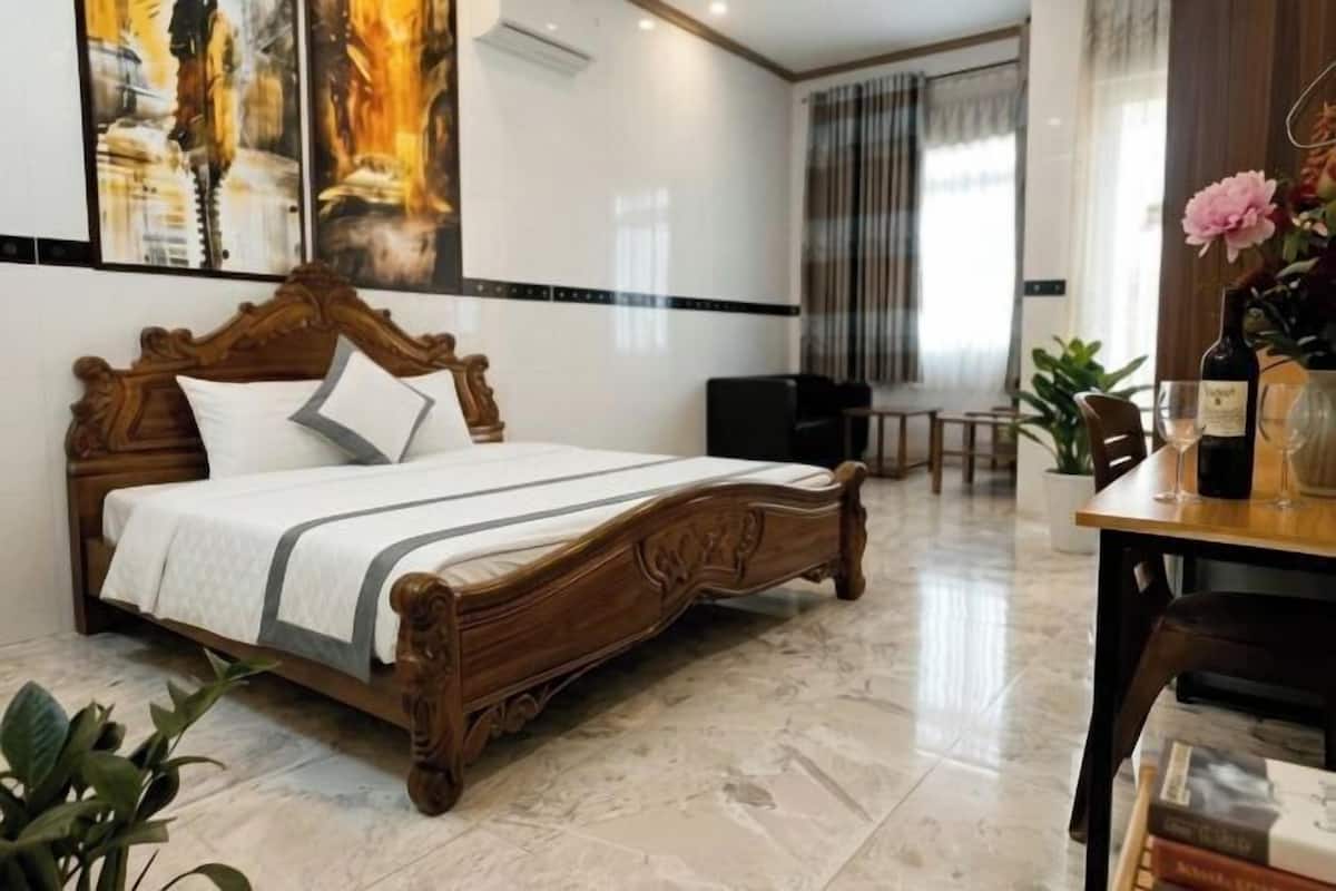 Une chambre d’hôtel avec un lit en bois, une table à manger avec des chaises, une plante en pot et un tableau au mur.