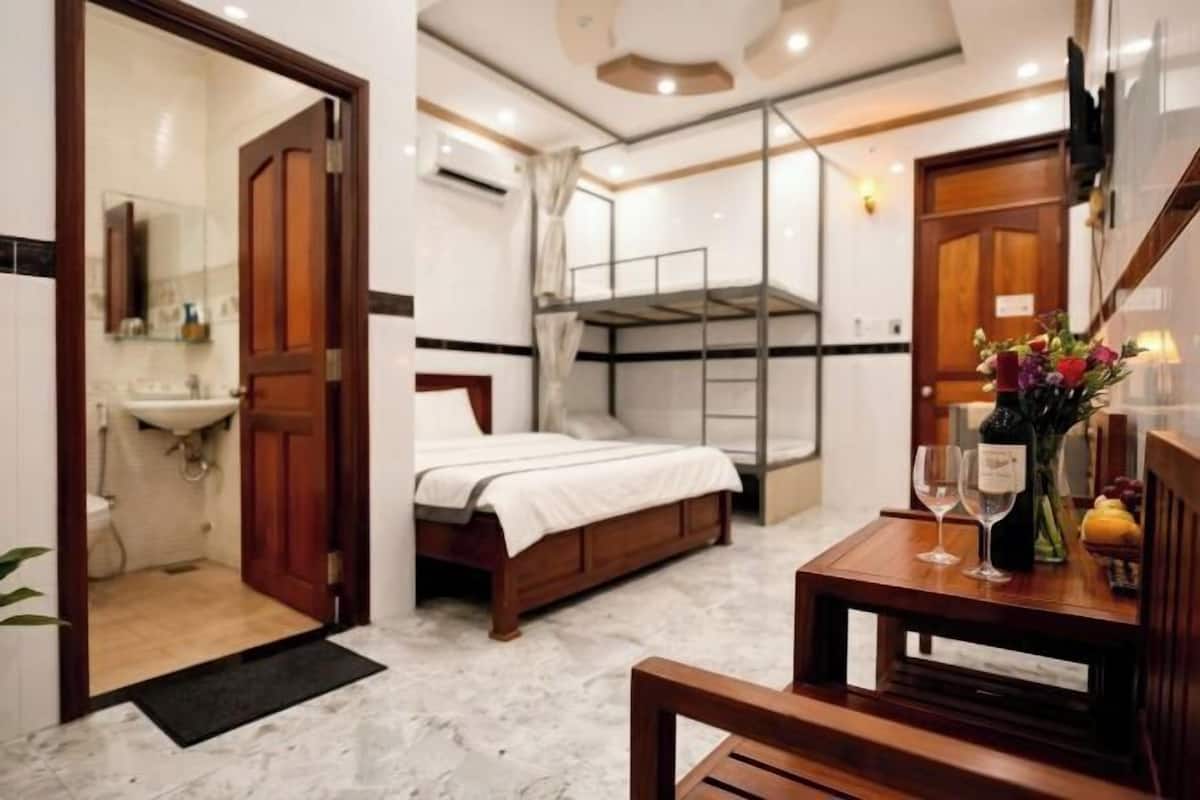 Une chambre avec un lit superposé, une table de chevet ornée d’un vase et de verres à vin, et une salle de bain avec un lavabo et un miroir.