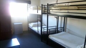 Quarto em dormitório com beliches, uma pequena escrivaninha e uma janela.