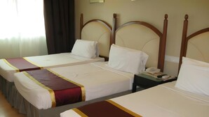 Ein Hotelzimmer mit drei Einzelbetten, jedes mit weißer Bettdecke und rot-goldener Dekoration.