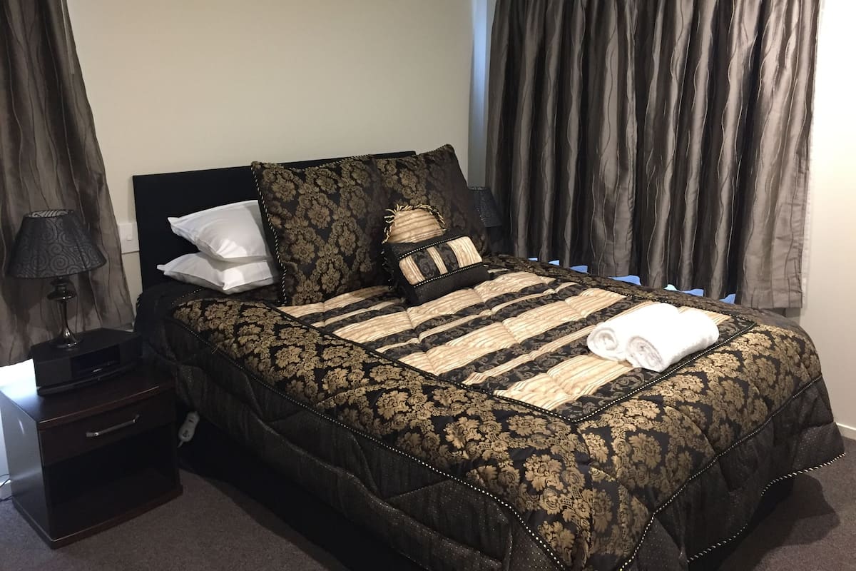 Una cama bien hecha con una colcha de diseño negro y dorado, dos almohadas y una toalla doblada sobre la cama.