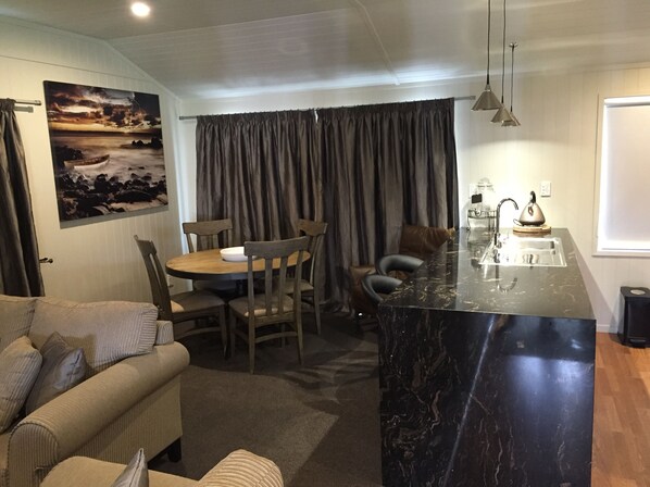 A compact living space with a dining area, a sofa, a kitchen island, and a painting on the wall. - Rocky Mountain Chalets (Ohakune)