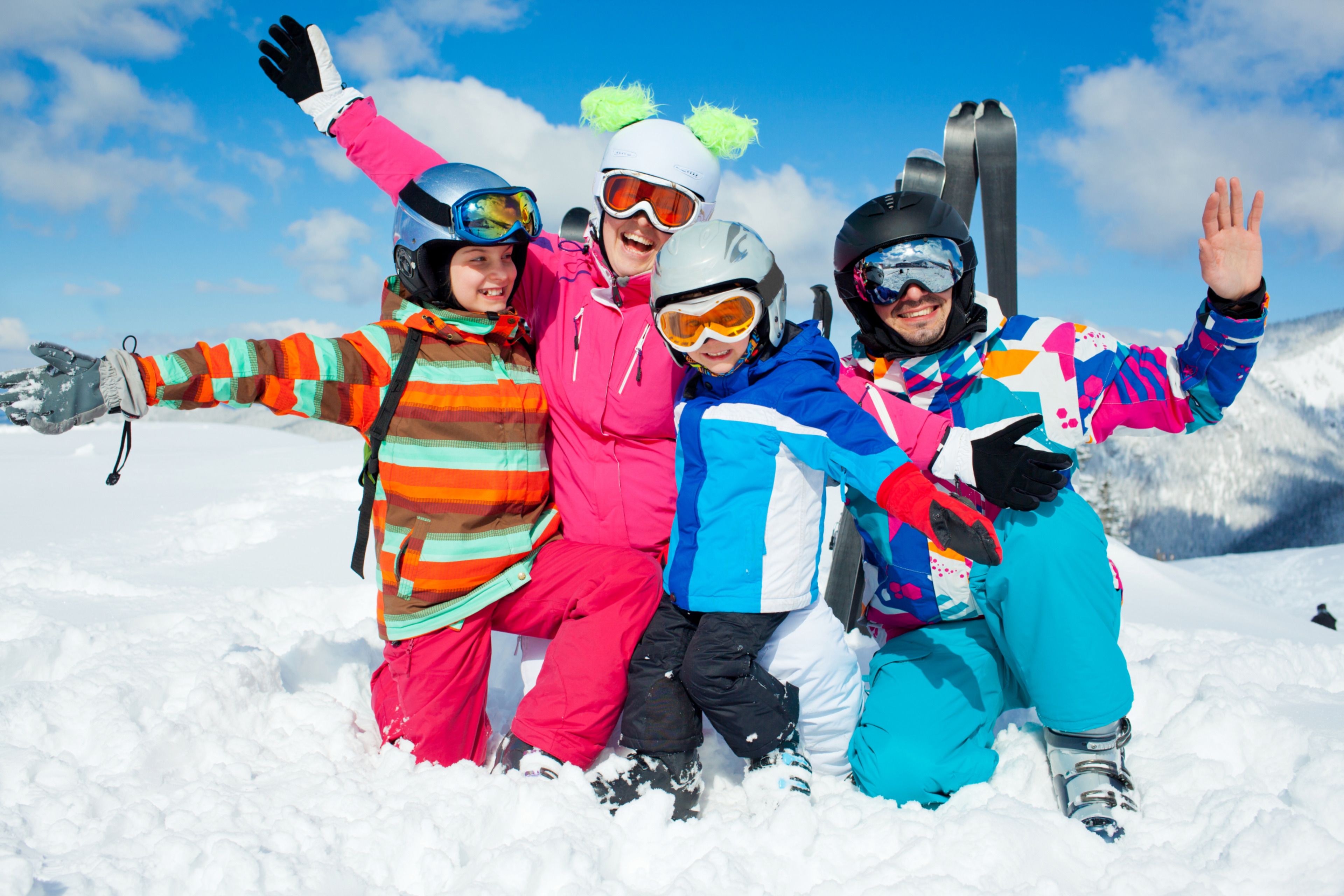 A group of people in colorful winter clothing posing on a snowy mountain with skis in the background.