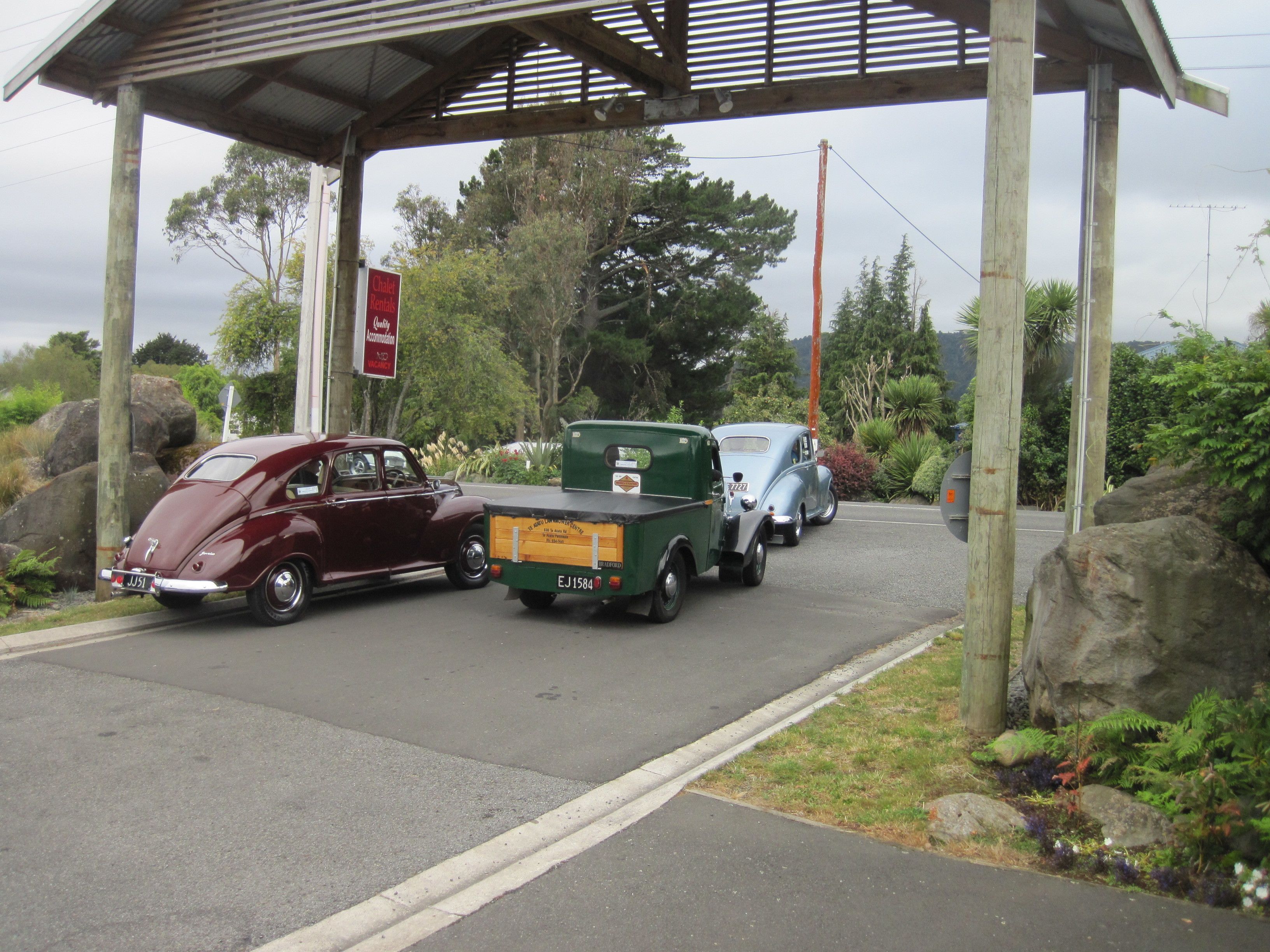 A vintage car and a truck parked under a shelter with a signboard.