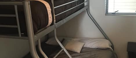 Un lit superposé avec une structure en métal, un lit simple en dessous et une fenêtre avec des stores.