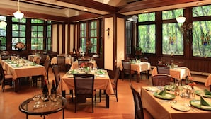 Un restaurante con varias mesas dispuestas para comer, con un ambiente cálido que incluye vigas de madera y ventanas amplias.