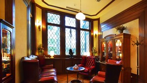 Una habitación con sillones de cuero, piso de madera, un aparador con puertas de vidrio y una ventana con vista a follaje.