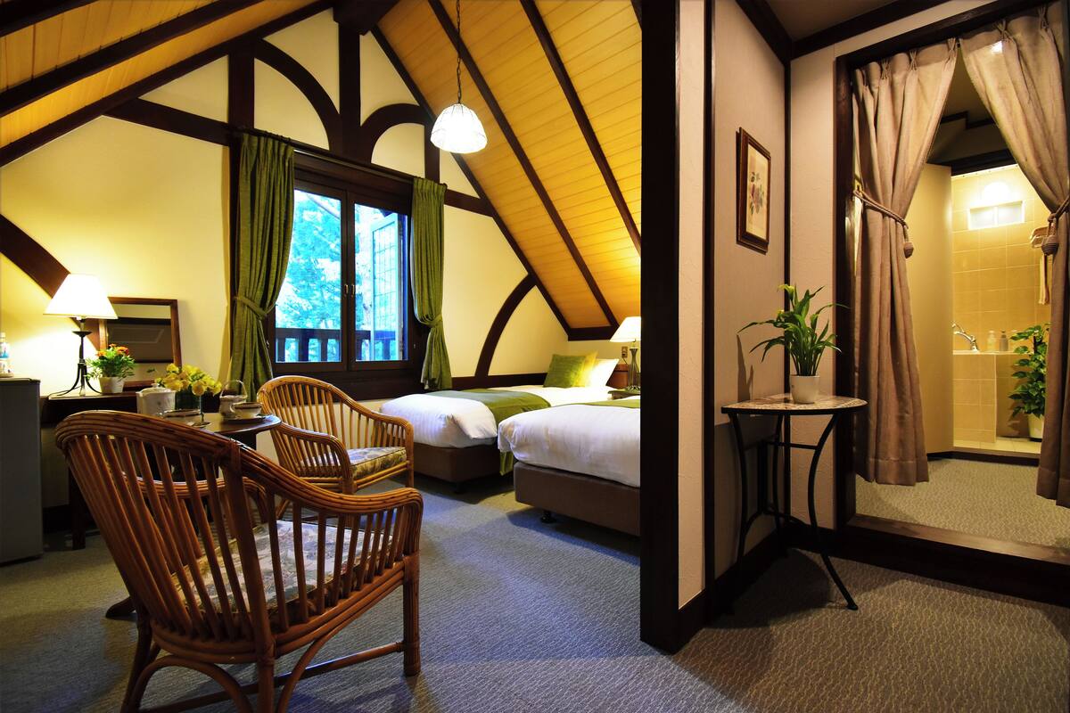 A cozy room with a bed, two chairs, a small table, and a window with curtains.